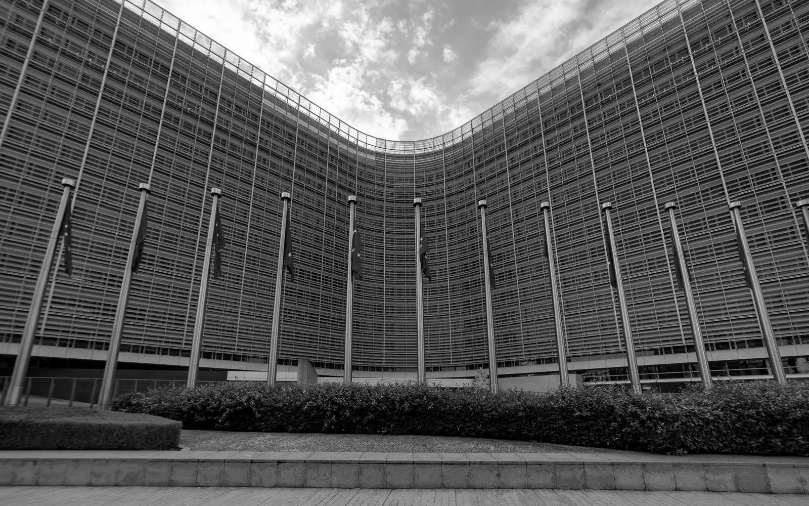 The curved facade of the Berlaymont building in Brussels with a row of EU flags, in black and white